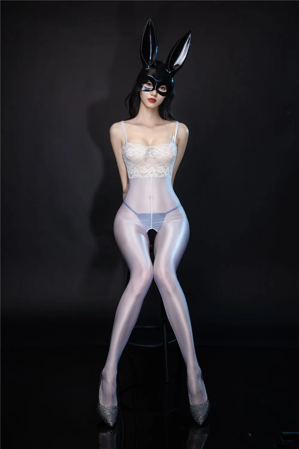 A woman posing in a white crotchless bodystocking featuring adjustable shoulder straps, a square neckline, white floral lace bodice, and glossy, close-footed leggings.