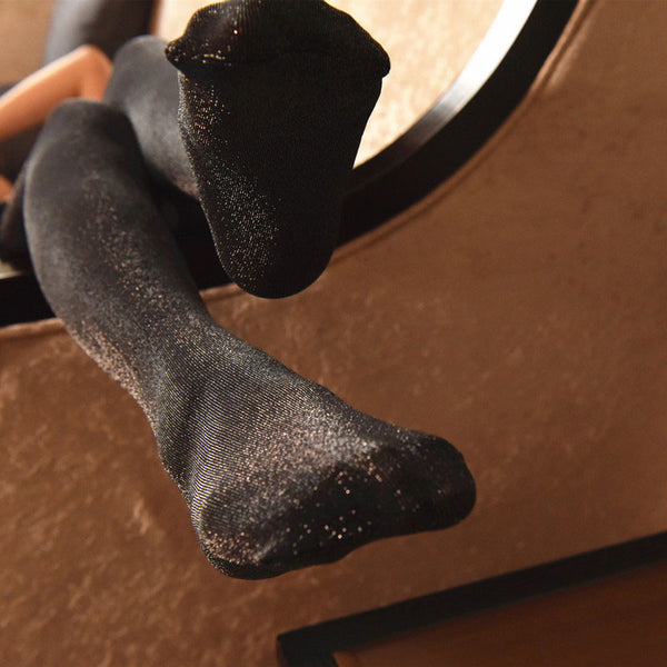 Close up view of lady feet wearing black shiny lace top thigh high stockings.